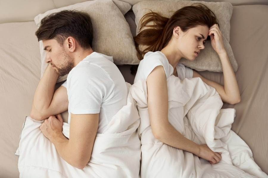 Casal deitado na cama de costas um para o outro, representando a questão de coisas mal resolvidas que podem causar doenças psicossomáticas